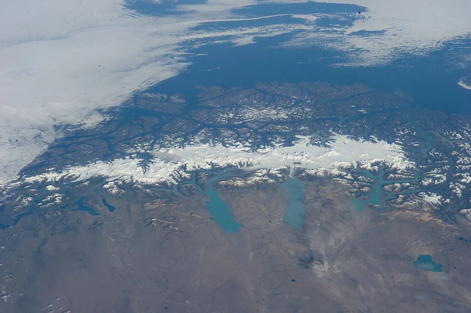 Photograph from orbit: a long white band of ice runs along the spine of the southern Andes, with turquoise glacial lakes to its east.